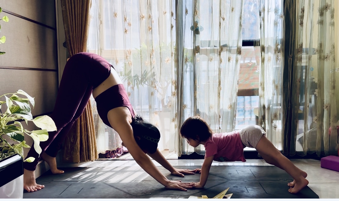 Hai mẹ con cùng tập tư thế chó úp mặt trên thảm, nắng chiếu qua rèm cửa